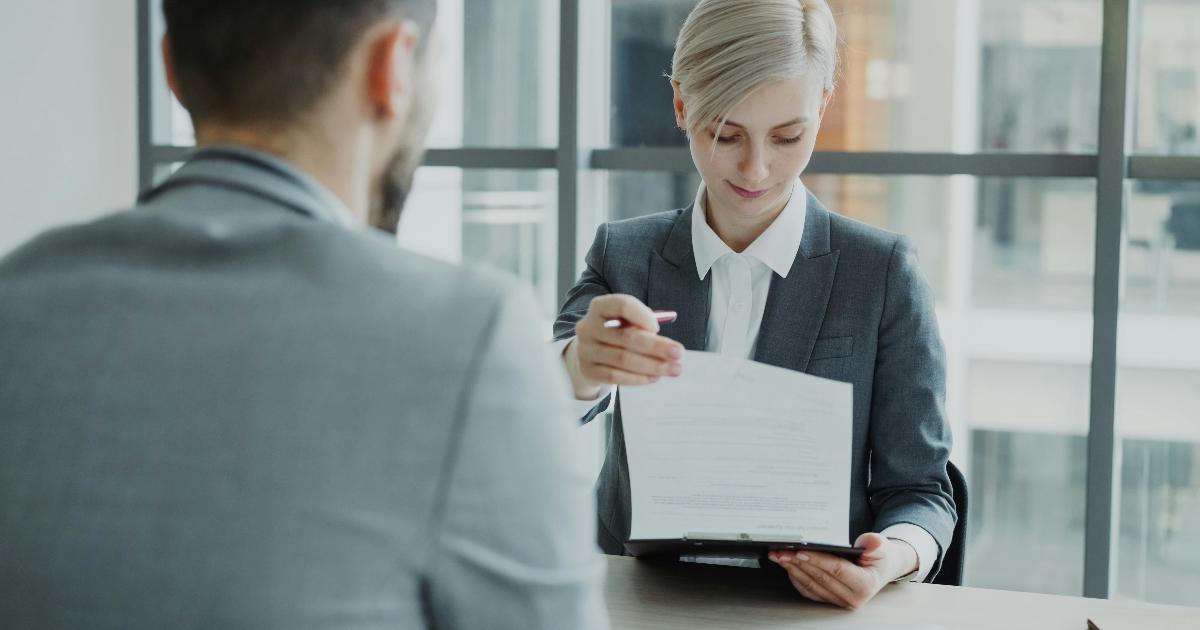 A hiring manager reviewing resumes next to a laptop, illustrating a degree requirement as an untested assumption in the hiring process.